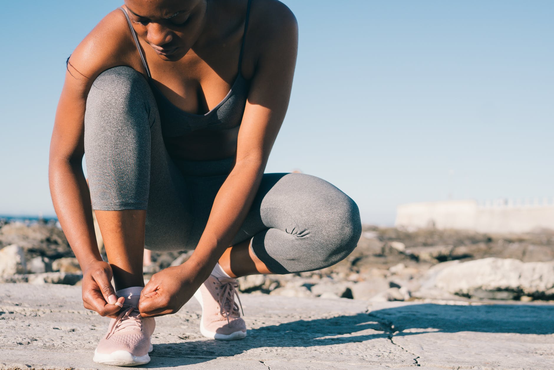 close up photo of woman in gray tank top and gray leggings tying her shoes