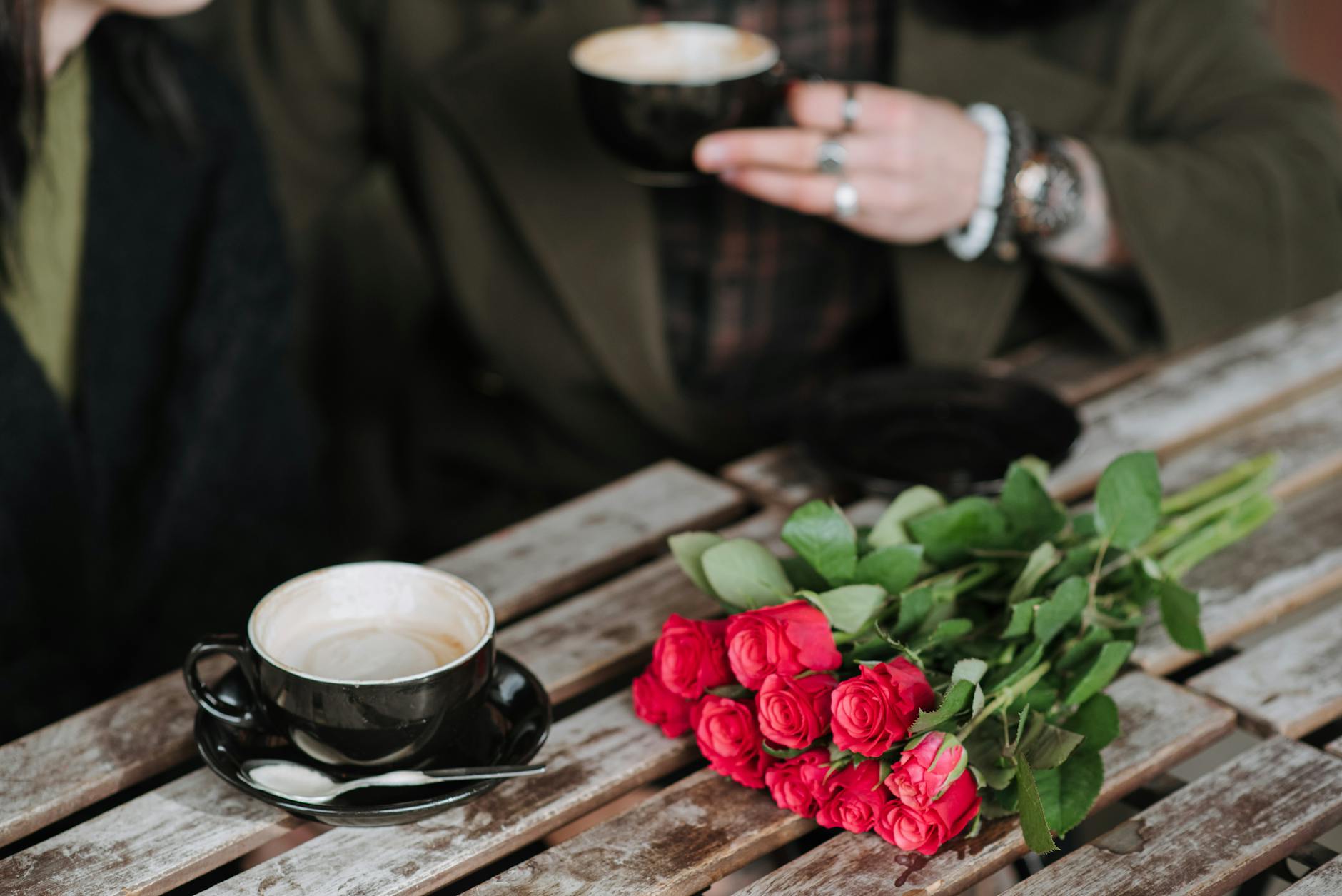 crop couple with cups of coffee and roses in cafeteria