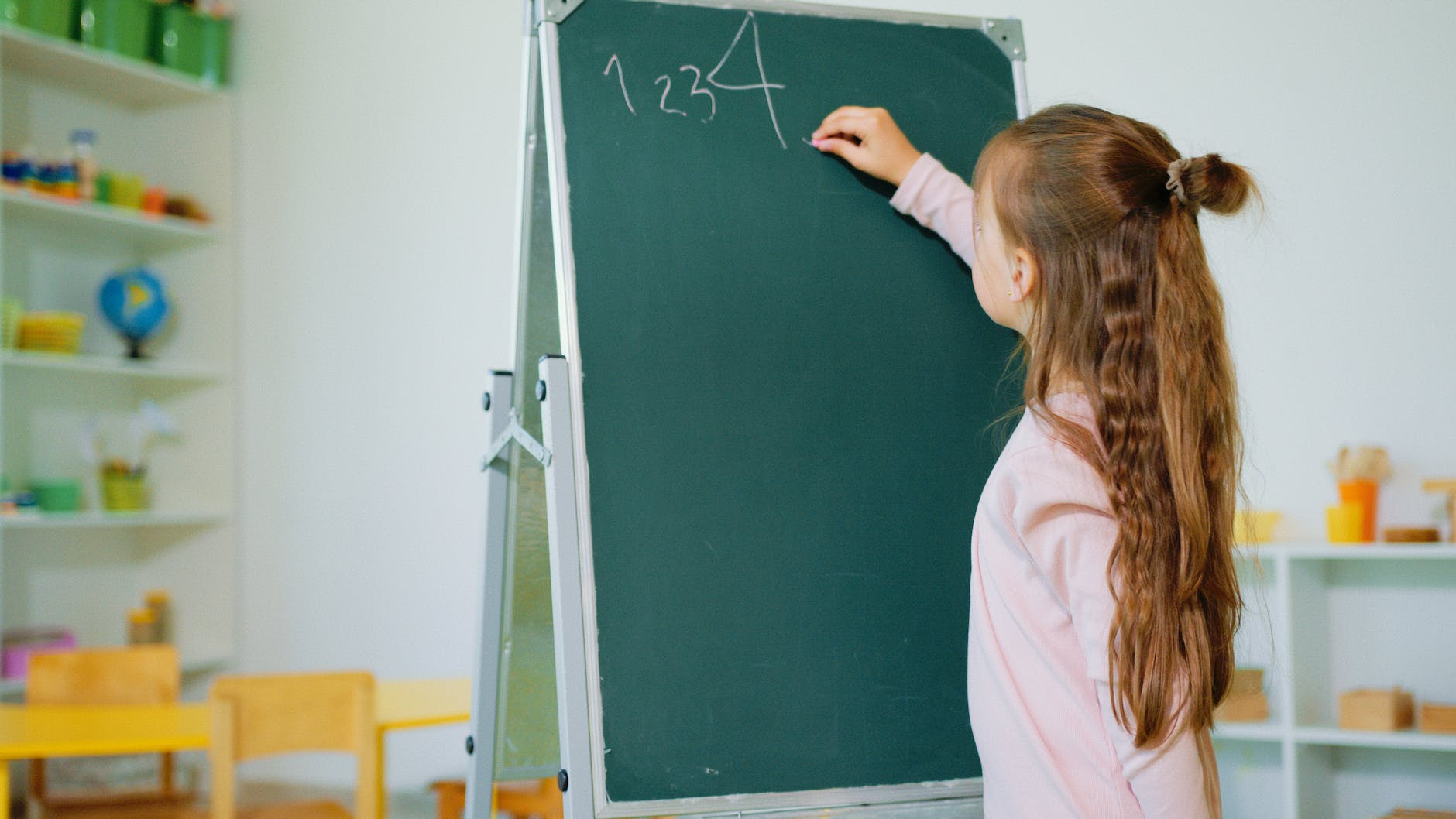 a girl in pink long sleeve shirt writing numbers on a chalkboard